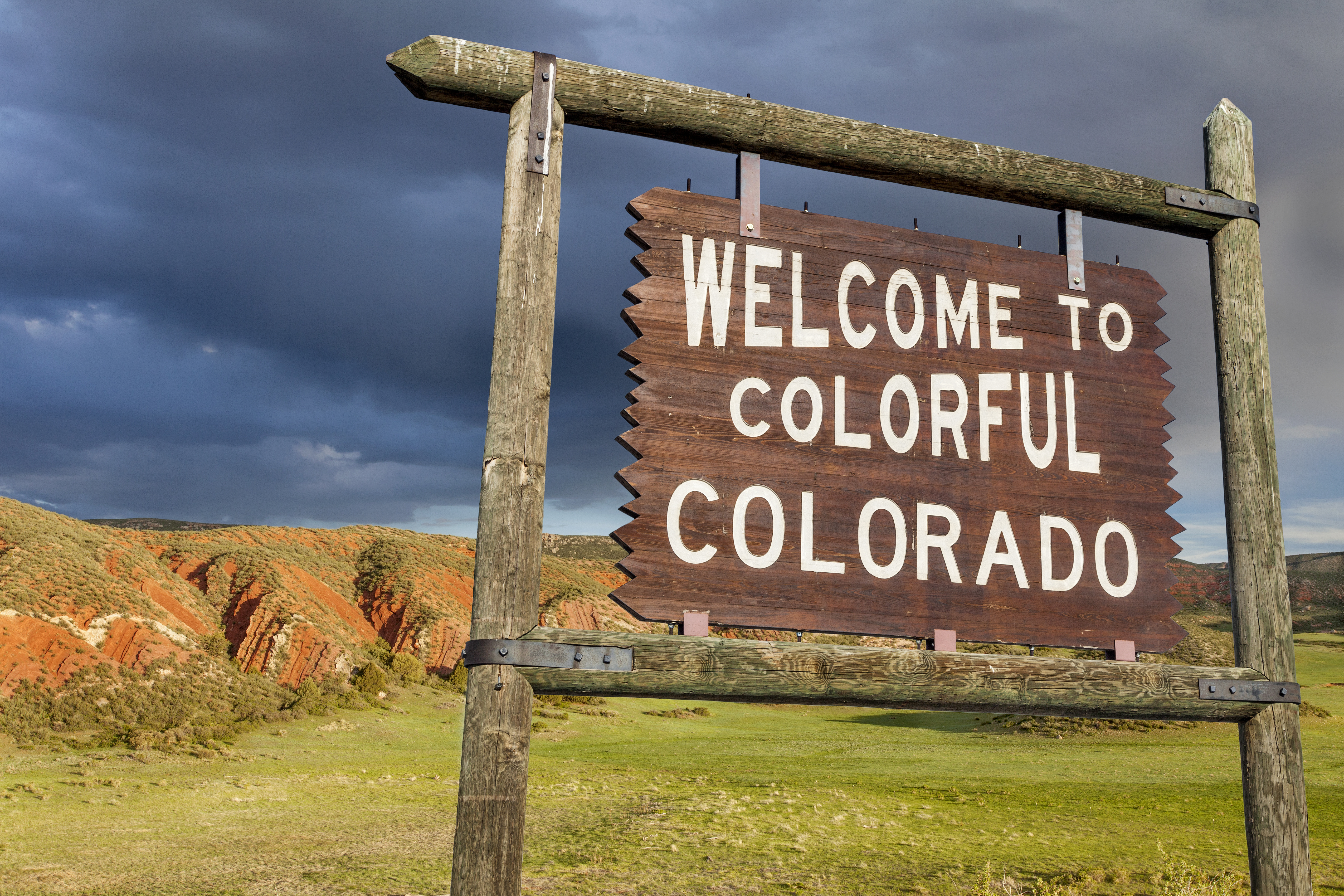 welcome to colorful Colorado roadside wooden sign with red sandstone cliff in background